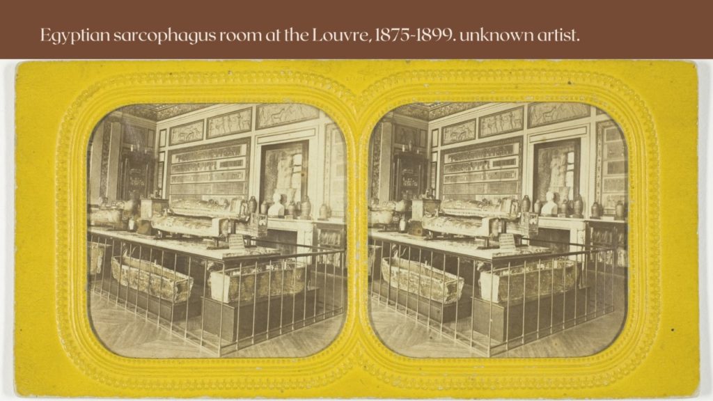 A stereoscopic photograph of a museum display, with Egyptian sarcophaguses displayed raised at different levels on a table and plinths, behind railings. The display is crowded. Busts and reliefs are visible on the walls and mantelpiece in the background, from floor to ceiling. The images are presented in their embossed yellow stereoscope card. 