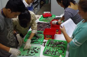 A photo of five people working with specimens on trays in a museum store. One is checking a list; the others are handling the items with gloves.